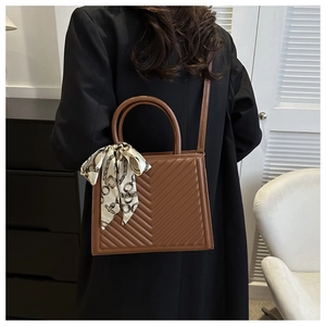 Détail d'un sac à main matelassé marron avec foulard en soie sur un manteau noir