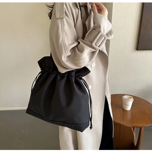 Detail of a large black drawstring bucket bag with stitching on a khaki trench coat