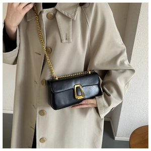Detail of minimalist black crossbody bag with gold hardware and chain strap on beige coat