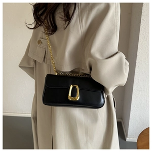 Close-up of black leather crossbody bag featuring a trapezoidal gold metal lock and chain strap