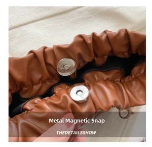 Detail of magnetic hardware closure and pleated leather edges on brown tote bag