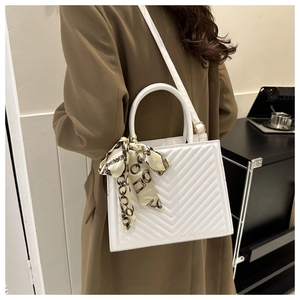 Detailed view of white quilted tote bag with decorative silk scarf on a brown coat