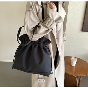 Detail of a black nylon drawstring tote bag with褶皱 design worn with a stylish trench coat
