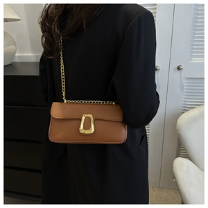 Brown faux leather crossbody bag with gold chain strap and geometric buckle on black coat