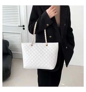 Close-up of white quilted leather tote bag with gold chain strap on a black blazer