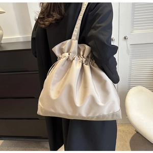 Detail of a large beige drawstring bucket bag featuring a soft satin texture and round base