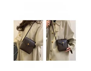 Detail of dark brown leather mini bag with lychee texture and golden buckle on beige trench
