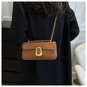 Brown leather crossbody bag with gold U-shaped buckle on black blazer background