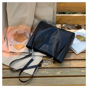 Detail einer schwarzen Kroko-Handtasche mit silberner Kette auf einer Holzbank
