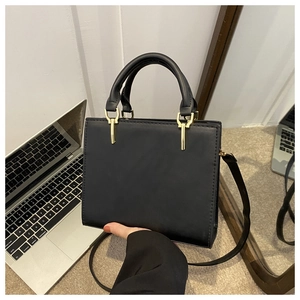 Detail view of textured black handbag with gold hardware and adjustable strap handles