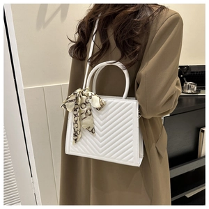 Détail d'un sac à main carré blanc à surpiqûres en V avec un foulard décoratif en soie