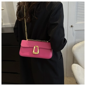 Detail of rose pink leather crossbody bag with gold U-shaped buckle and metal chain strap