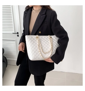 Dettaglio borsa shopper trapuntata bianca con catena dorata su giacca nera elegante