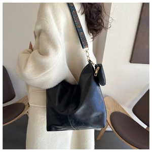 Detail of black leather hobo bag with ethnic jacquard strap on a white coat model