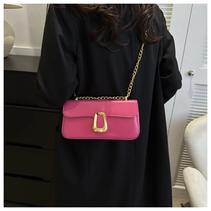 Close-up of bright pink leather crossbody bag with golden chain on a black coat