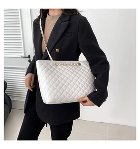 Detailed view of white quilted tote bag with gold chain strap and diamond stitching pattern