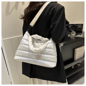 Detail of white quilted puffer bucket bag with wide shoulder strap worn by a model