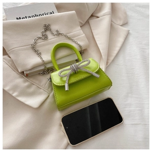 Close-up of mini lime green handbag with rhinestone bow showing size relative to a phone