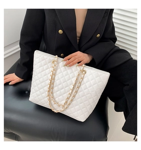 Close-up of white quilted tote bag with golden metal chain straps on a model