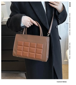 Detail of a brown quilted tote bag with gold hardware worn with a black wool coat