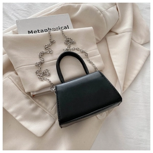 Detail of elegant black mini crossbody bag with silver chain strap on chic suit
