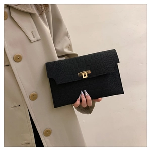 Close-up of black crocodile-embossed envelope clutch with a gold twist-lock on a coat