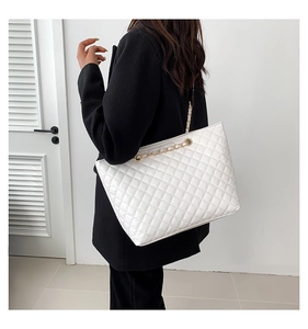 Detail of white quilted faux leather tote bag with gold chain strap on model shoulder