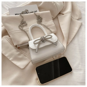 Detailed view of white mini handbag featuring a sparkling rhinestone bow and silver chain