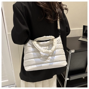 Detailed view of white quilted puffer bucket bag with wide handle and metal hardware