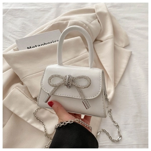 Detail of white leather mini bag with sparkling rhinestone bow and silver chain strap