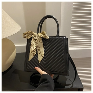 Détail d'un sac à main noir à surpiqûres en V avec un foulard décoratif sur la poignée