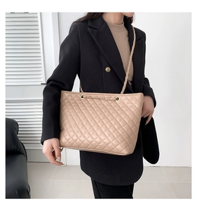 Dettaglio borsa shopper beige trapuntata con catena dorata indossata da modella in interno