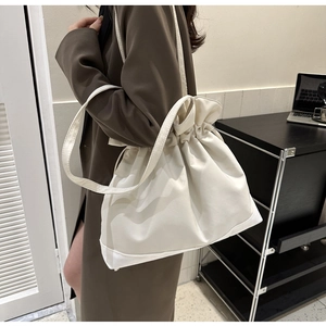Detail of a creamy white drawstring tote bag featuring soft pleated textures and stitching