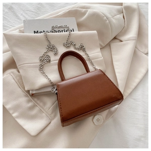 Detail of a brown leather mini trapezoid bag with top handle and silver chain strap