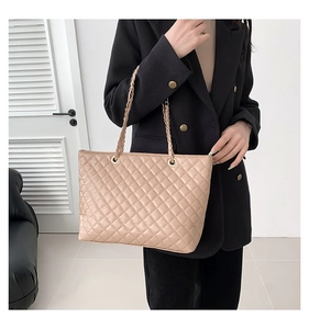 Detail of beige quilted tote bag with golden chain straps shown on a black suit blazer