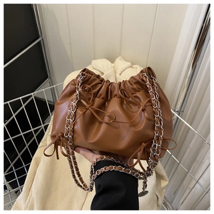 Detail view of brown pleated bucket bag featuring delicate bows and silver chain strap