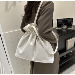 Detail of a large cream drawstring tote bag with soft leather texture and long shoulder strap