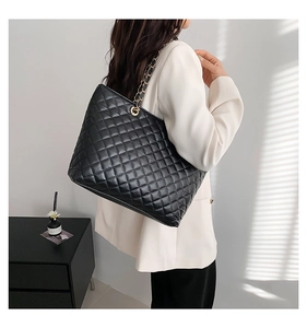 Detailed view of black quilted tote bag with golden metal chain strap on model shoulder