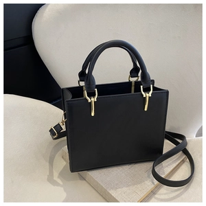 Detail of a black square handbag with matte leather finish and golden metal accents