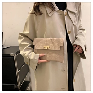 Detail of stone-pattern envelope clutch bag with gold metallic twist lock on a beige coat