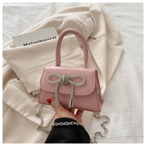 Detail of pink leather mini bag featuring a dense silver rhinestone bow and chain strap