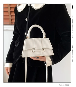 Detail of white textured striped handbag with golden ring buckle on black jacket
