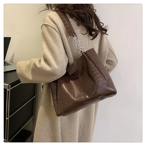 Detail einer dunkelbraunen Kroko-Handtasche mit silberner Kette an der Schulter