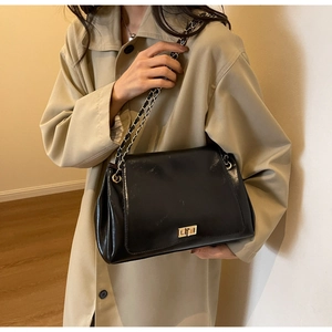 Detail of black glossy faux leather shoulder bag featuring gold chain and turn-lock closure