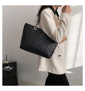 Detail of black quilted tote bag with golden chain strap on a model for daily commute