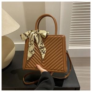 Détail d'un sac bandoulière matelassé caramel avec foulard en soie élégant et poignée
