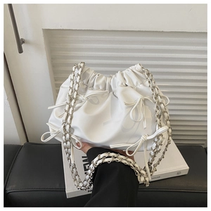 Detail of white pleated bucket bag with bow tie and silver chain strap on books