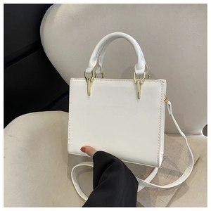 Close-up of a white leather handbag featuring gold metal hardware and a round handle