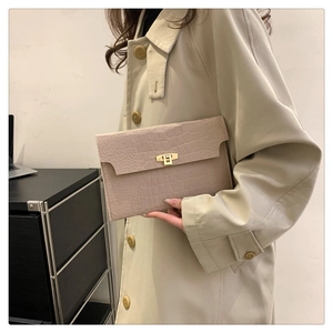 Detail of beige crocodile pattern clutch with gold metal twist lock on a trench coat