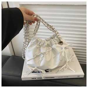 Close-up of white ruched cloud bag featuring decorative leather bows and silver chain strap